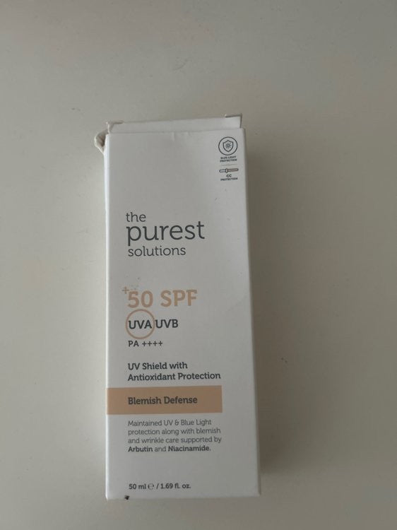 واقي شمس من ماركة "the purest solutions". الصندوق بلون كريمي هادئ، ومكتوب عليه بوضوح "Blemish Defense" مع عامل حماية "50 SPF